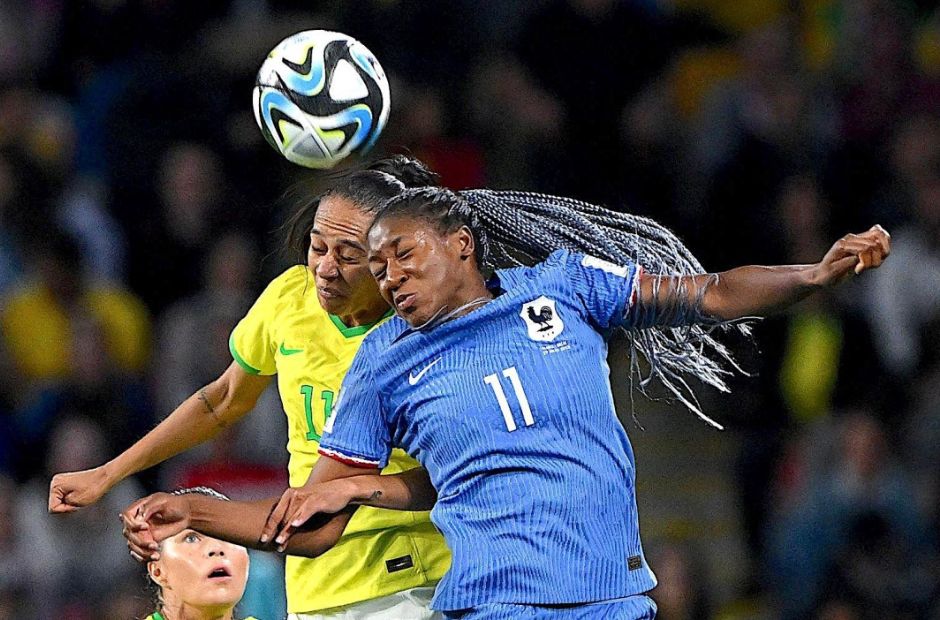 Cầu thủ Pháp trong trang phục màu xanh đang nhảy lên tranh chấp bóng với cầu thủ người Brazil trong trang phục áo vàng